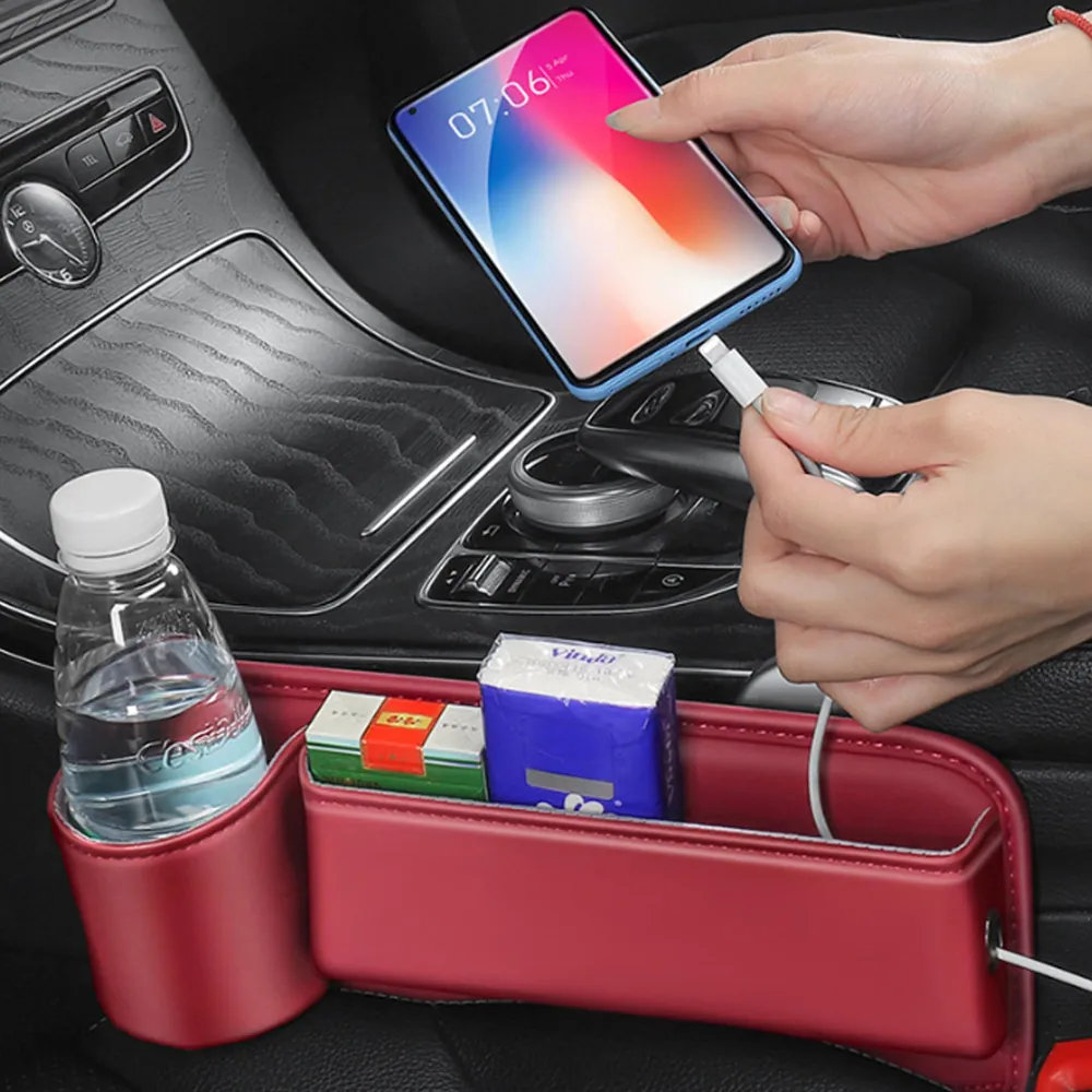 A red seat gap organiser fitted beside a car seat, holding a phone on charge and a bottle